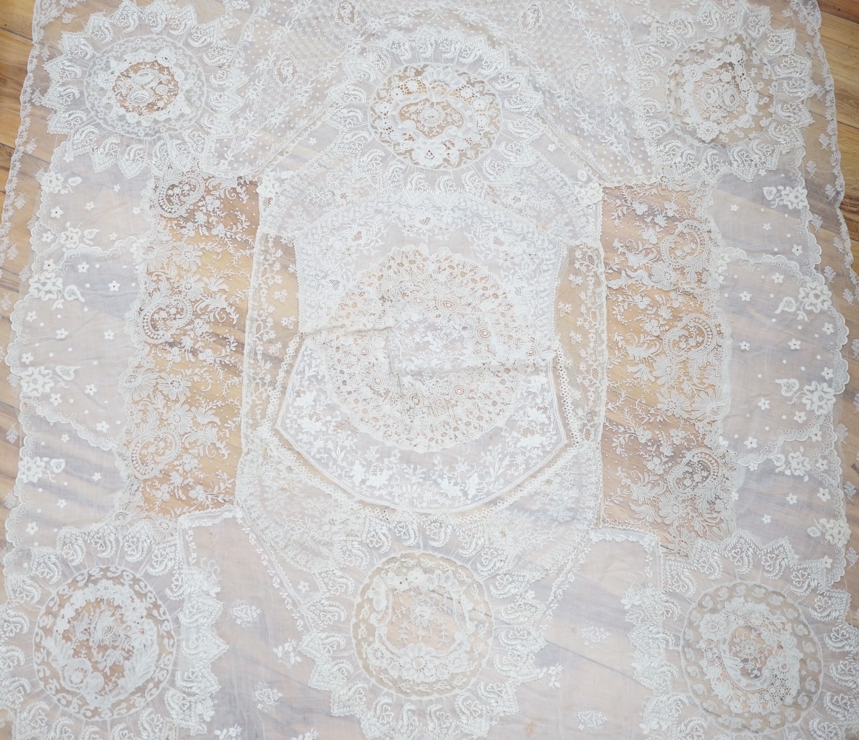 A late 19th century Normandy lace table cover of hand spun linen, hand white worked, with Brussels Point de Gaze insertions and bobbin lace edging, together with two feathers and a net veil